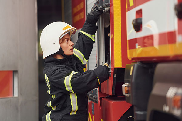 A firefighter in gear retrieves equipment from a fire engine compartment.