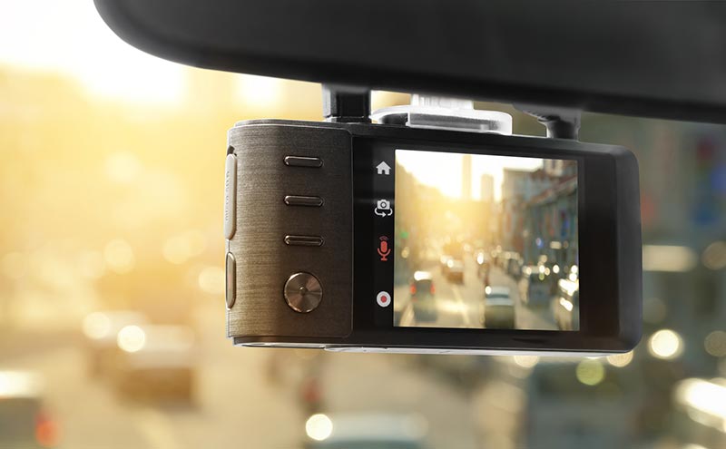Close-up of a car dashboard camera with a screen displaying a sunny city street with vehicles.