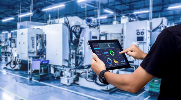 A person manages IIoT systems and navigates data charts on a tablet in an industrial setting.