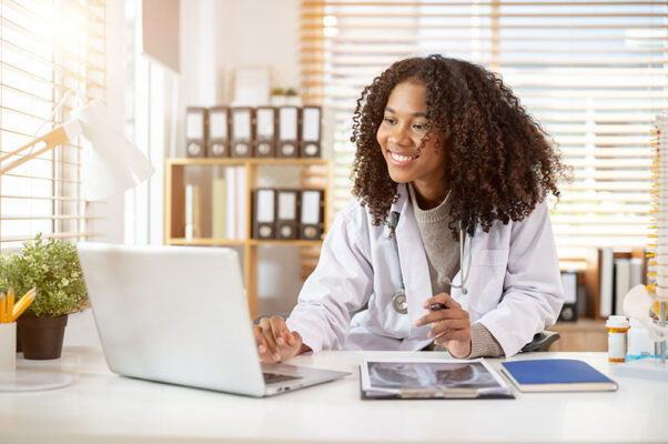 In a well-lit office, a doctor smiles at a laptop.