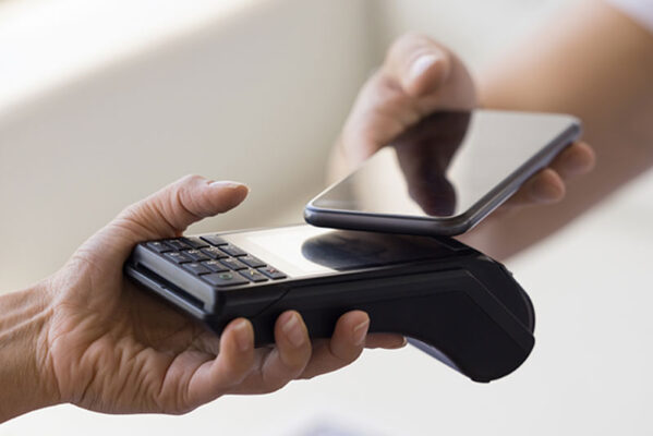 A person makes a contactless payment using a smartphone over a card reader. Payment systems rely in in-factory profile provisioning for local MNOs subscriptions.