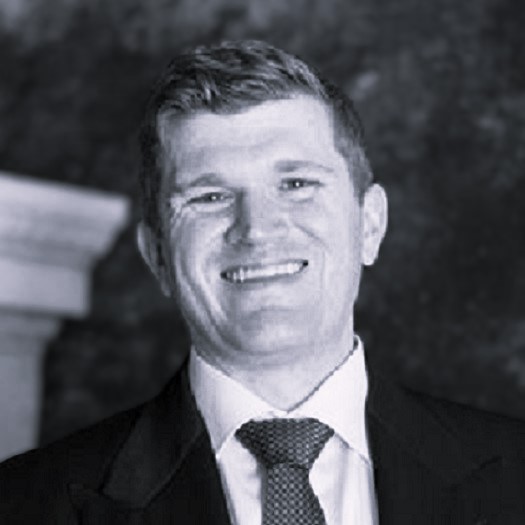 Smiling man in a suit and tie, standing against a dark background.