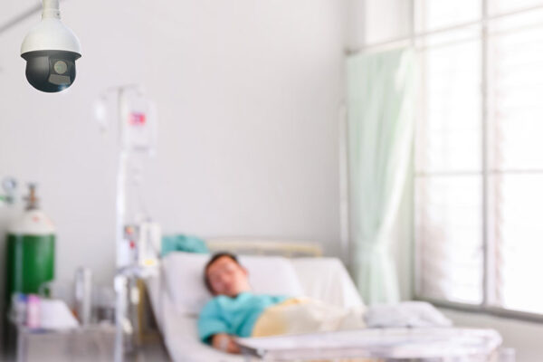 In a connected health care setting, a surveillance camera quietly observes a patient lying in bed, surrounded by advanced medical equipment.