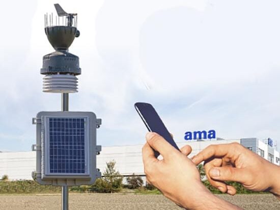 A hand holds a cell phone near an antenna in front of a building.