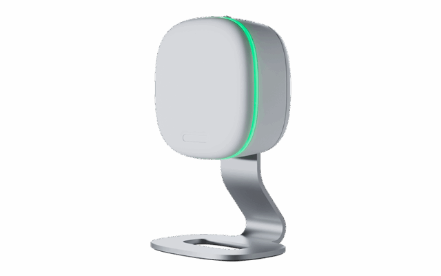 A small, white, rectangular Vitalthings electronic device with rounded edges, mounted on a silver metal stand, featuring a green LED light along its side.
