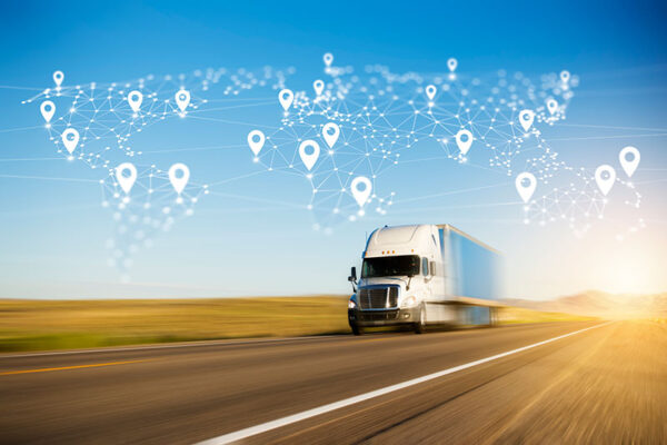 A semitruck drives on a highway with a digital world map in the sky overlaid with location markers, showing the global potential of IoT telematics and tracking solutions.