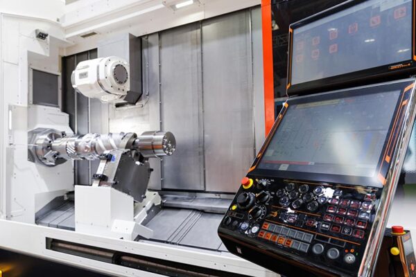 A CNC machine with a metal workpiece mounted for machining, alongside a control panel displaying operational settings.