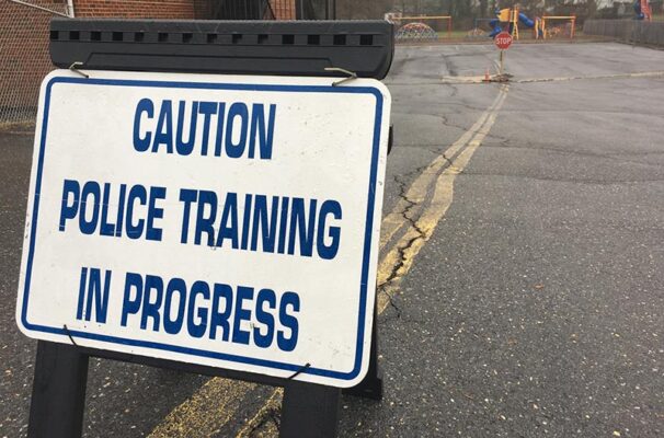 A sign reading "Caution Police Training in Progress" stands over yellow double lines painted on asphalt.