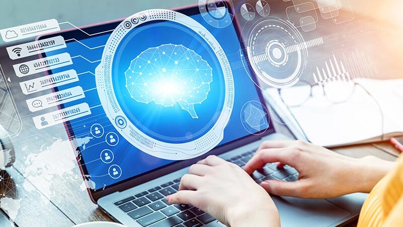 A person types on a laptop displaying a digital brain, data icons and technology graphics.