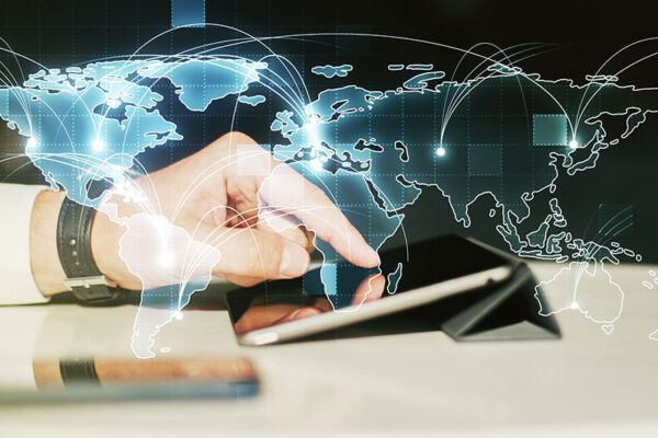 A glowing world map with digital network lines representing global IoT is superimposed over a hand using a tablet.
