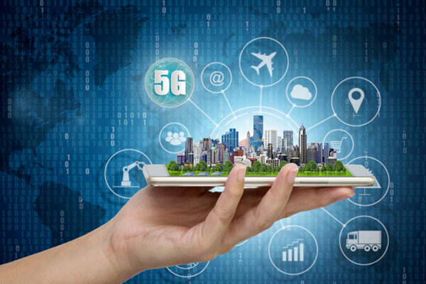 A hand holds a smartphone displaying a miniature cityscape, with 5G and other digital network icons in the background.
