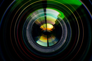 Close-up view of a camera lens with colorful reflections and concentric circles visible on the glass surface.