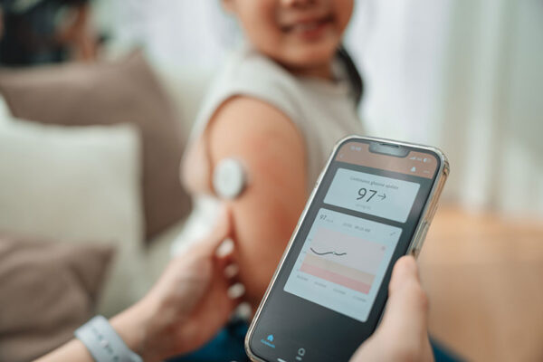A person scans a sensor on a child's arm with a smartphone, powered by 5G RedCap IoT, showing a blood glucose level reading of 97 and a graph on the screen.