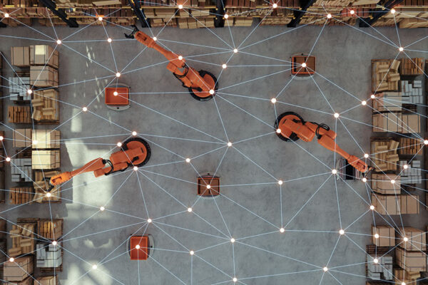 Overhead view of three robotic arms in a warehouse with shelves, connected by a digital network overlay.