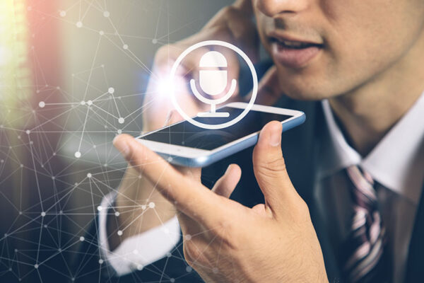 A man holds a smartphone near his mouth, speaking into it, with a digital microphone icon and network graphics superimposed over the image.