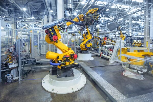 Large industrial robots assemble components on an automated production line in a modern factory with metal structures and bright lighting.