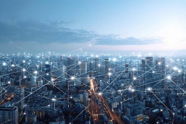 A cityscape at dusk with illuminated buildings and digital lines connecting points, representing network connectivity and smart city technology.