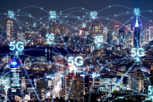 A cityscape at night with illuminated buildings and digital 5G network icons overlaid, symbolizing widespread 5G wireless connectivity.