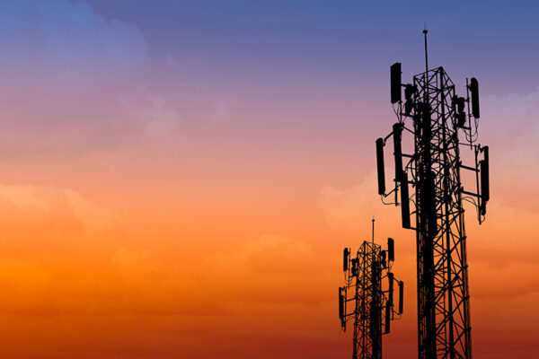 Two cell towers stand against an orange and purple sky.