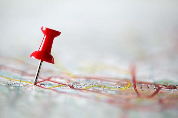 A red pushpin is stuck into a paper map covered with red and yellow lines, marking a specific location.