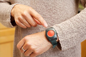 A person presses the button on a black wristband featuring a large red emergency alert button.