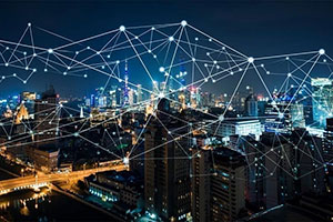 A cityscape at night with illuminated buildings, overlaid by a network of connected lines and dots representing digital or wireless connectivity.