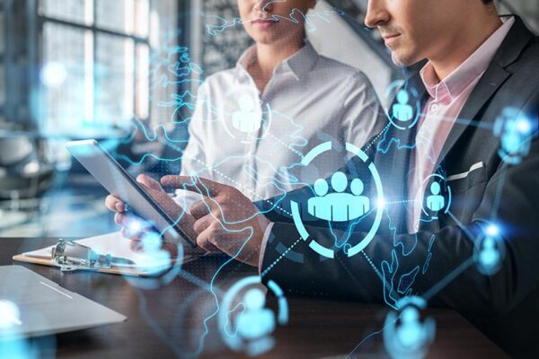 Two business professionals use a tablet, with digital network and global connection graphics overlayed, representing members of an IoT R&D team.