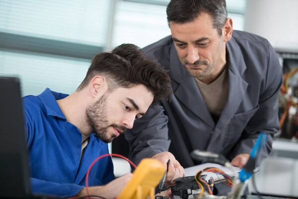 Two technicians inspect electronic components on a workbench.