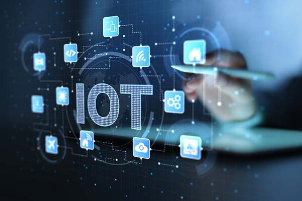 A person using a stylus on a tablet screen showing the text “IoT” surrounded by glowing digital network icons.